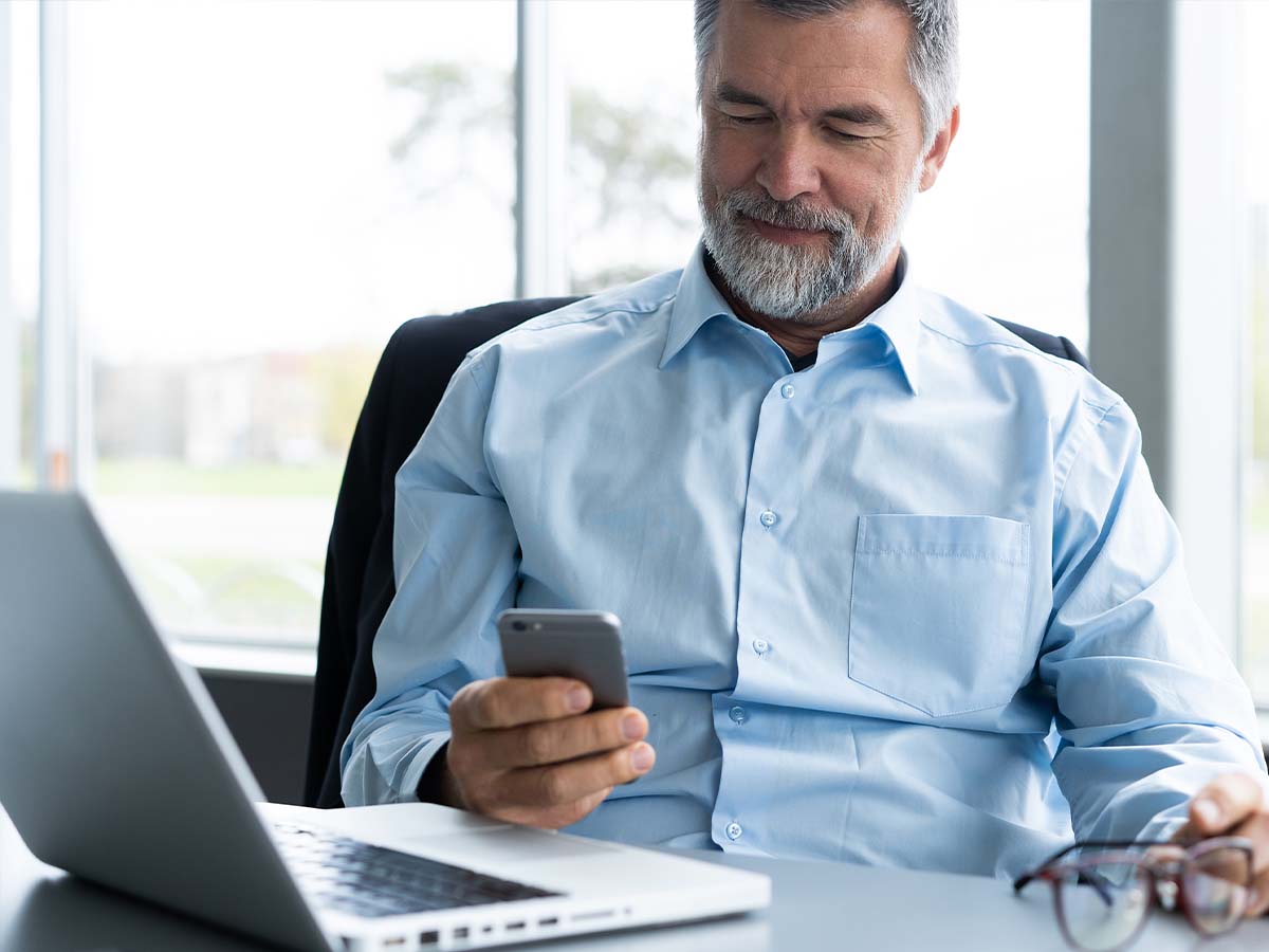 A man using a smartphone and a laptop in an office setting