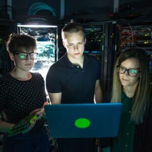 people standing around laptop in dark room