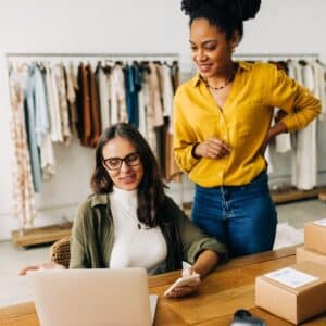women in boutique look at laptop with boxes on table