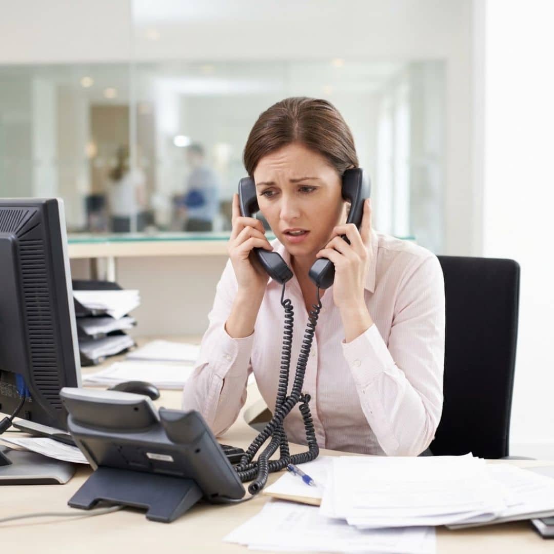 A stressed female receptionist overwhelmed by multiple tangled desk phone lines.