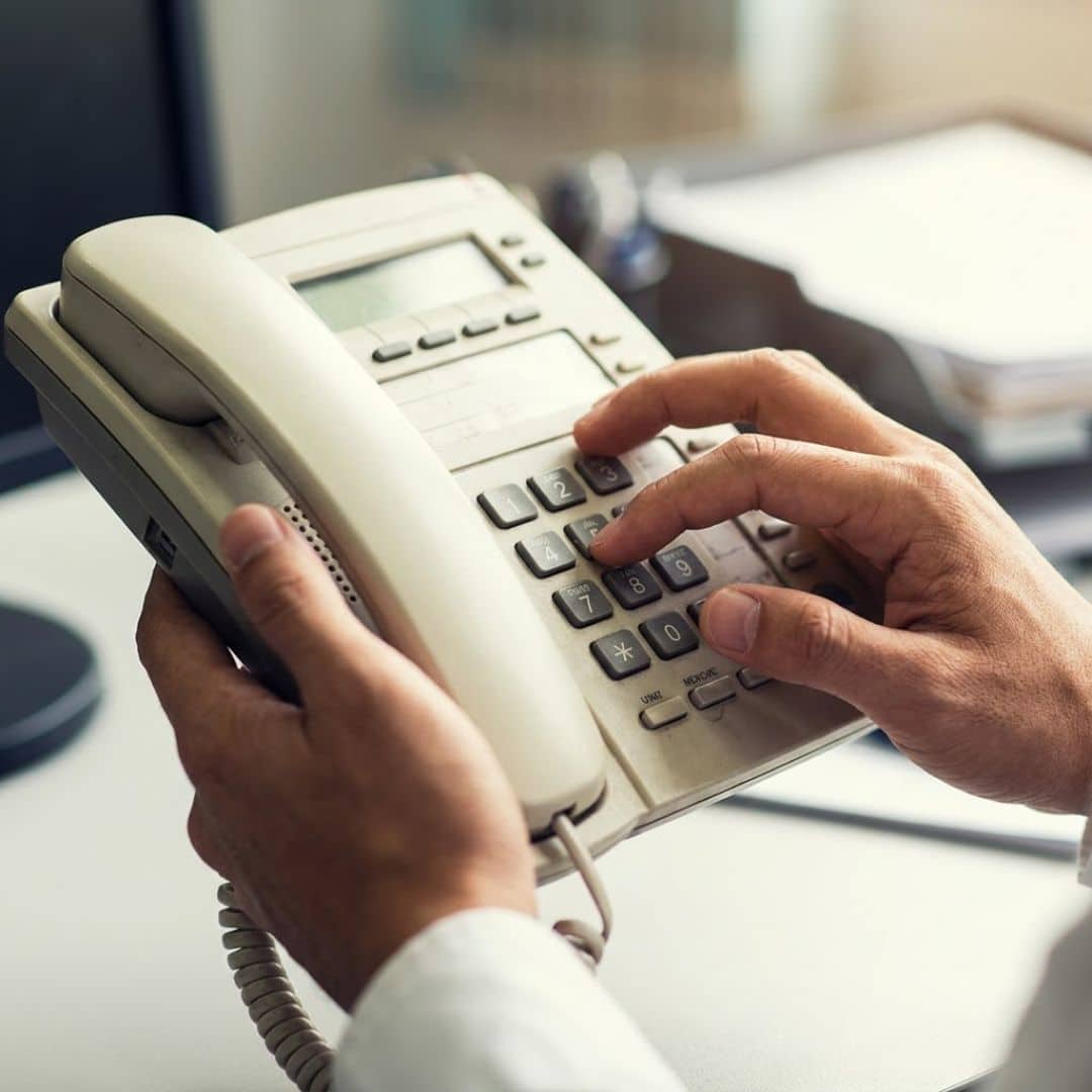 Confused fingers hover over the outdated push-button keys of a traditional business desktop phone, contrasting with the advanced technology seen previously.
